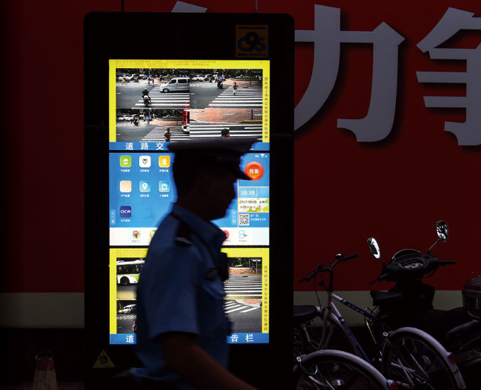 2017年8月9日，一名中國交通警察走過了上海路口的安裝的面部識別屏幕。（AFP）
