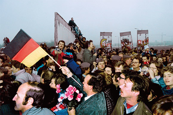 東德共產黨慶祝「國慶」40周年大閱兵之後一個月，柏林圍牆倒坍。圖為1989年11月12日，東德人手持國旗和鮮花湧進西柏林。（AFP）