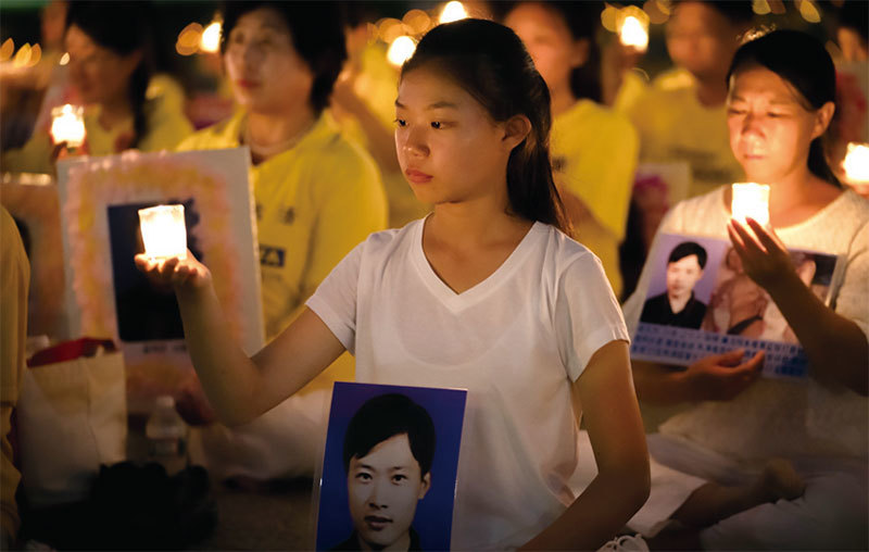 華府「720」法輪功反迫害燭光夜悼，來自遼寧的16歲女孩徐鑫洋手捧父親徐大為的遺像。徐大為因為堅持修煉法輪功被冤判8年監禁，出獄後13天離世。（石青雲／大紀元）