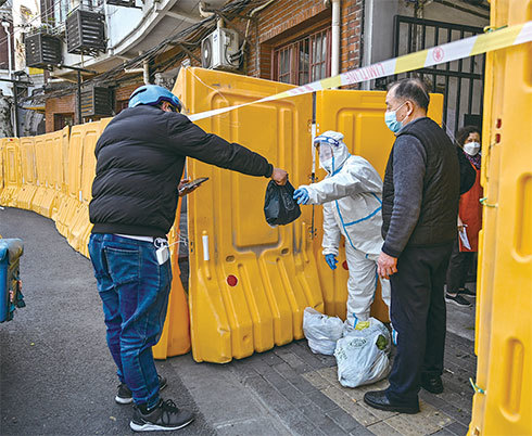2022年3月29日，上海靜安區，一名身穿防護裝備的工人守衛著一個處於封鎖狀態的社區入口，從一名送貨員手裡接收食物。（Hector Retamal/AFP）