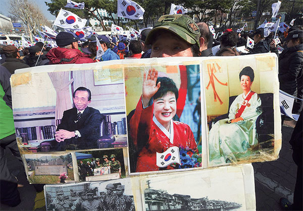  朴槿惠2017年3月21日在首爾中央地方檢察廳接受聆訊，支持者舉著朴槿惠（中）、她的父親朴正熙（左）和母親陸英修（右）的肖像聲援。（Jung Yeon-Je / AFP）