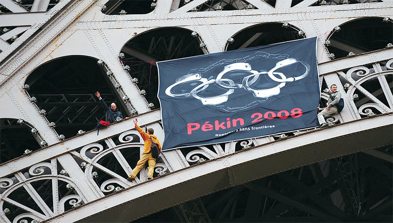 2008年4月7日，無國界記者組織活動人士在巴黎埃菲爾鐵塔上豎起一面旗幟，將五個奧運五環變成了手銬，抗議中共以奧運為藉口迫害人權。（Olivier Laban-Mattei / AFP）