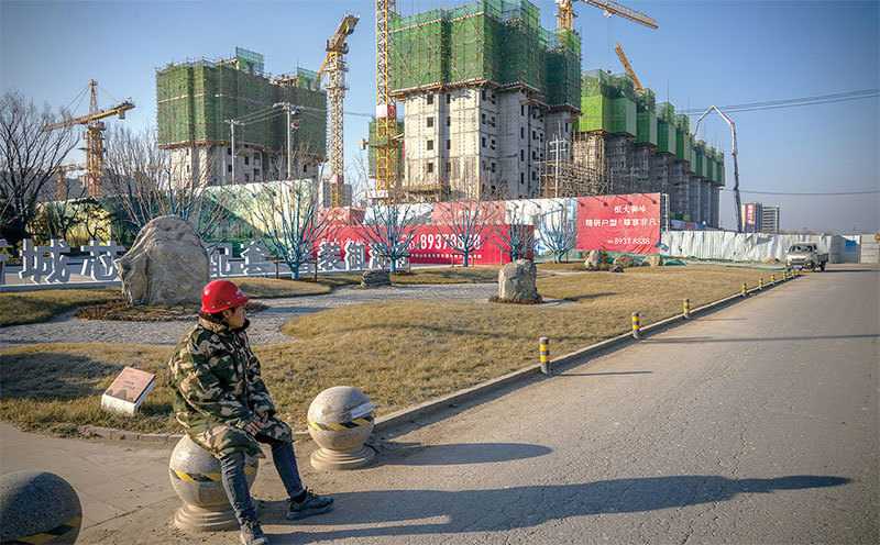 2022年1月6日，在中國北京，一名工人坐在中國恆大集團一個開發項目的施工現場的未完工的公寓樓前。（Andrea Verdelli / Bloomberg via Getty Images）