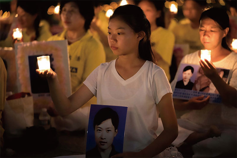 身穿白衣的徐鑫洋2017年7月參加美國華盛頓DC的燭光夜悼活動，她左手所持的是父親徐大為的生前照片。她身後是母親遲麗華。（石青雲／大紀元）