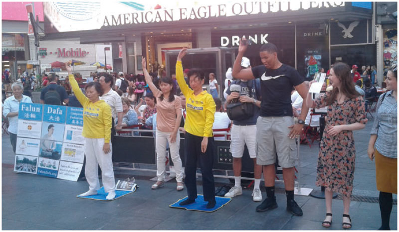 紐約時代廣場跟著法輪功學員學練功法動作的遊客。