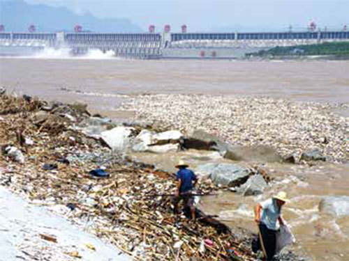 三峽上游山體坍塌、長江生態環境惡化……三峽周邊旱澇和地震等地質災害不斷。圖為2010年，長江三峽大壩附近的江面漂浮大量垃圾，兩名工人正在清理。（AFP）
